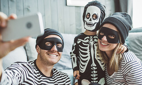 Two adults dressed as burglars with a small child dressed as a skeleton standing between them taking a selfie